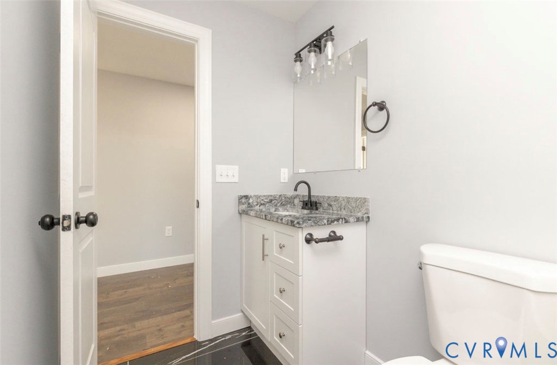 White cabinetry vanity with stone-finish countertop, undermount sink, matte black faucet, wall-mounted light fixture, and black floor tile