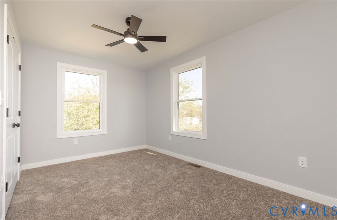 Neutral interior featuring wall-to-wall carpeting, dual windows, and a ceiling fan with integrated lighting