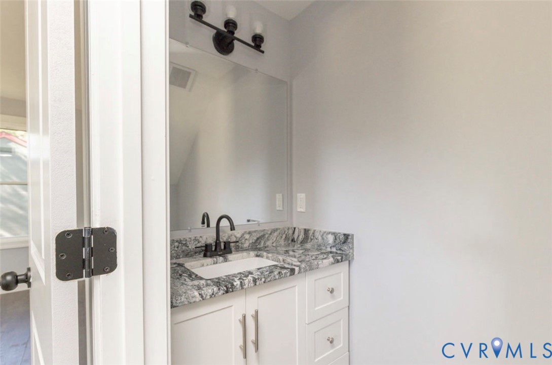 Bathroom vanity featuring a stone countertop, white cabinetry, a rectangular undermount sink, a matte black faucet, and a coordinating three-light vanity fixture