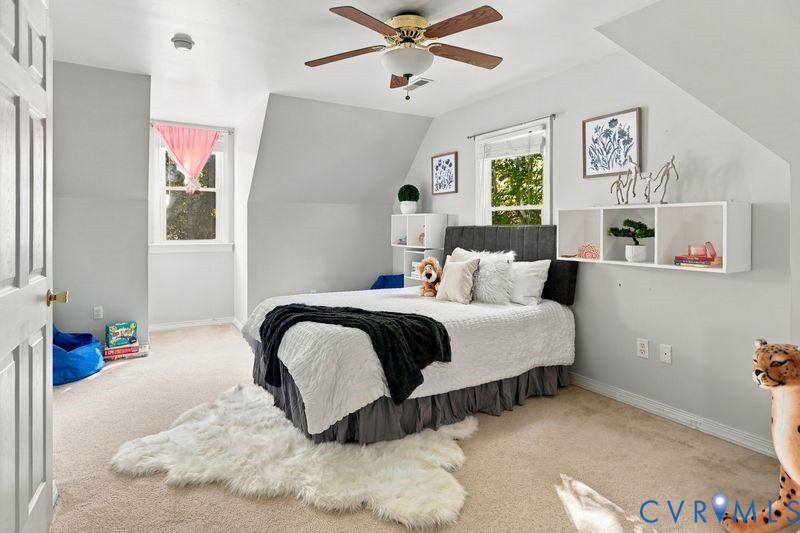 Bedroom featuring vaulted ceilings, wall-mounted white storage shelving, carpeting, and a central ceiling fan with integrated lighting