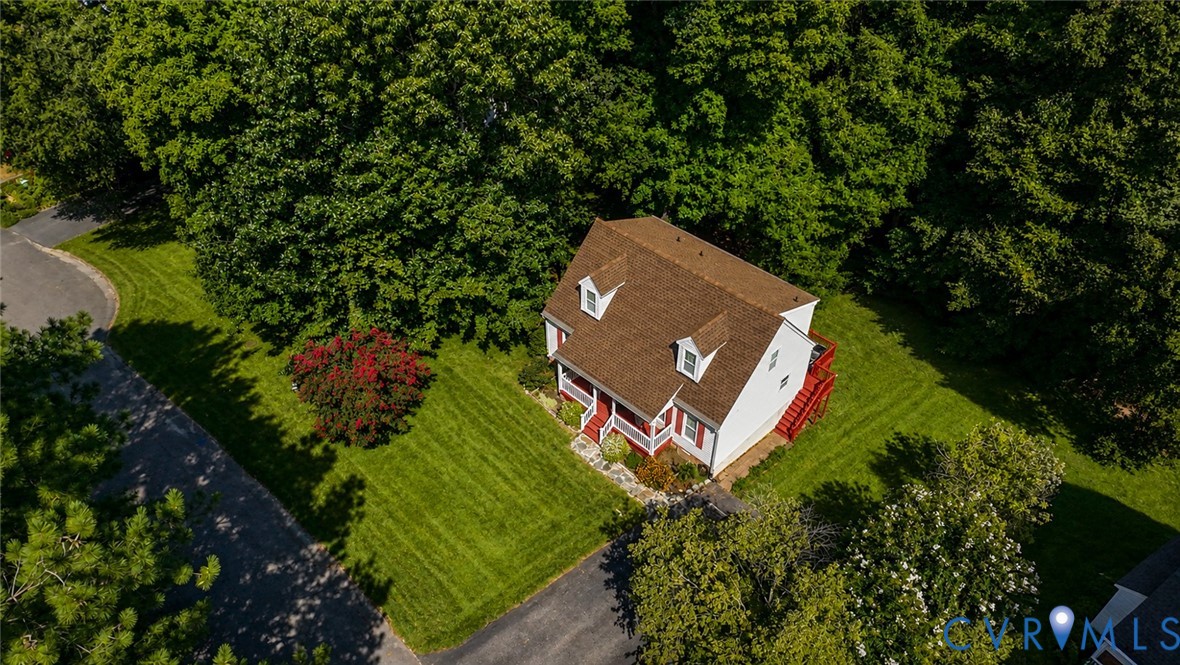 Two-story residence featuring a shingled roof, dual dormer windows, a stone-paved walkway, and a rear elevated deck, all situated on a lot with mature trees and maintained lawn
