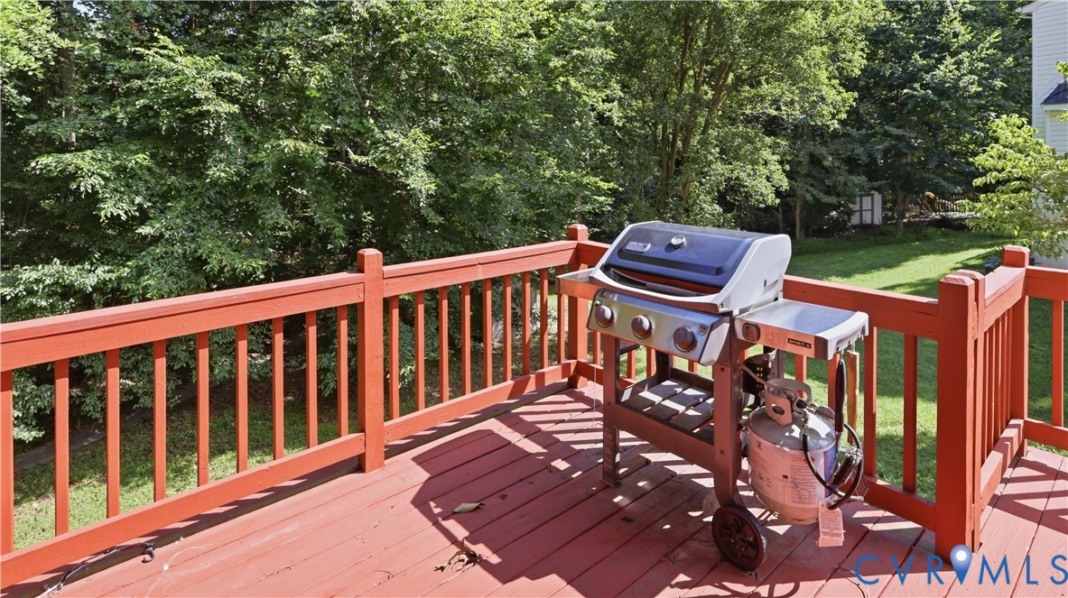 Raised wooden deck featuring vertical baluster railings and a grassy yard backdrop