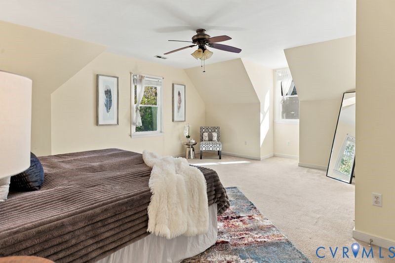 Room with neutral walls, sloped ceiling architectural detailing, carpeted flooring, multi-light ceiling fan, and windows