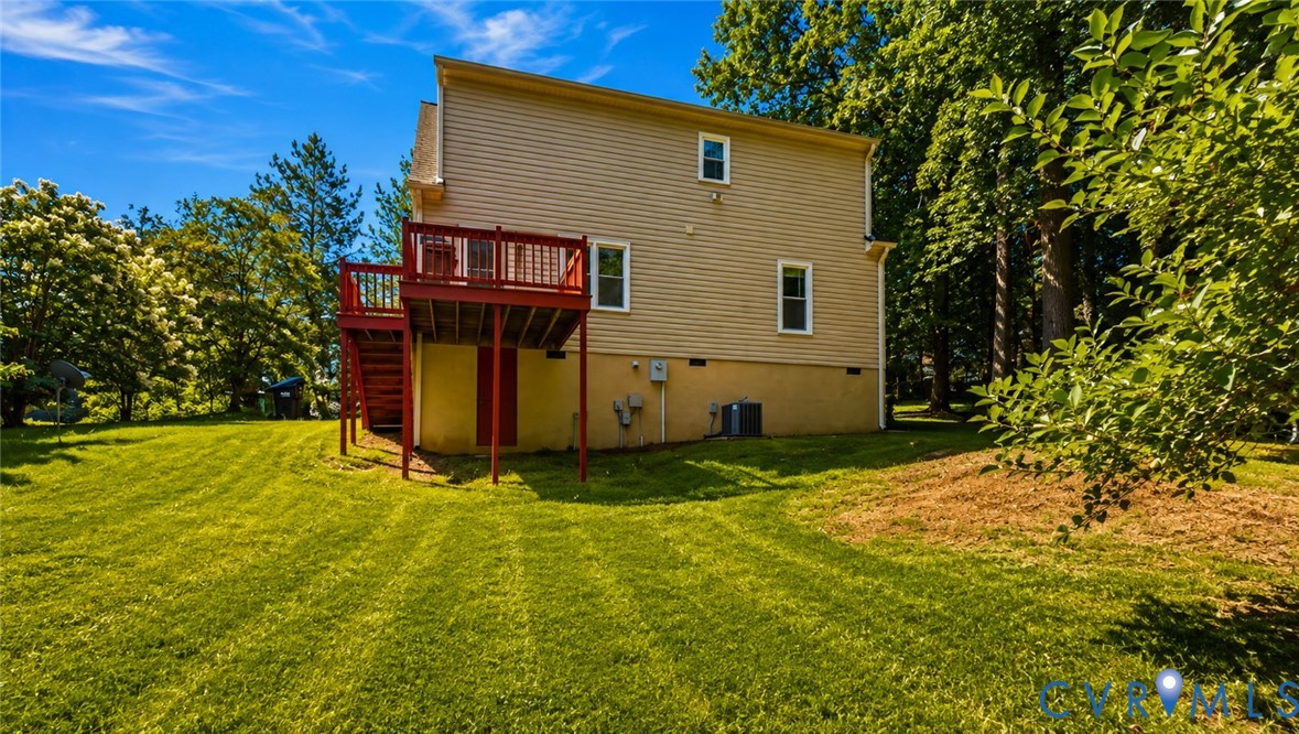 Two-story exterior featuring light-toned horizontal siding, a raised rear deck with stairs, a lawn, and mature perimeter trees