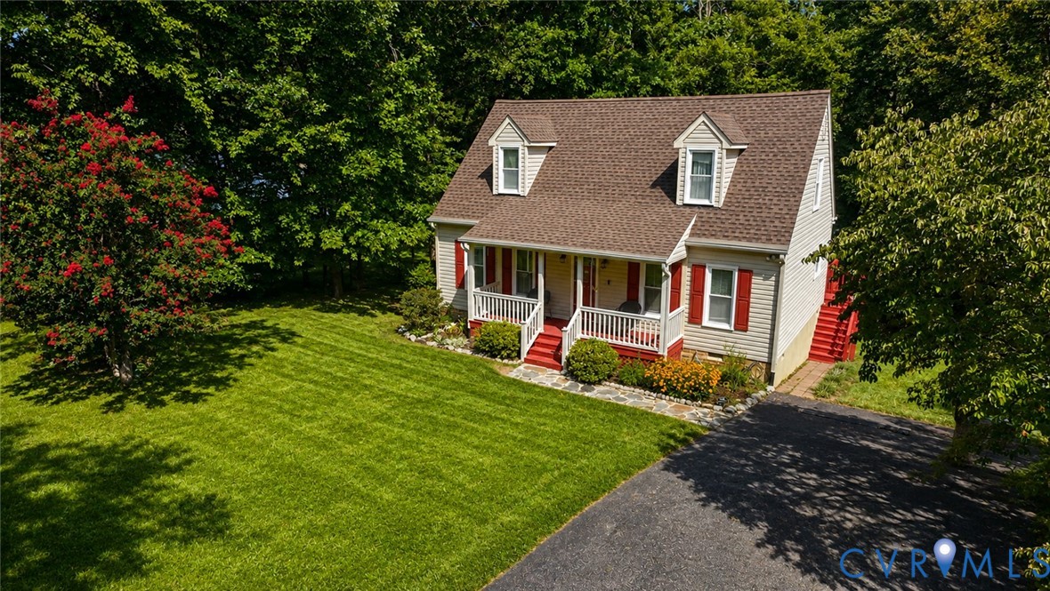Cape Cod style exterior featuring horizontal siding, twin dormer windows, a covered front porch with railings, a stone walkway, and an asphalt driveway