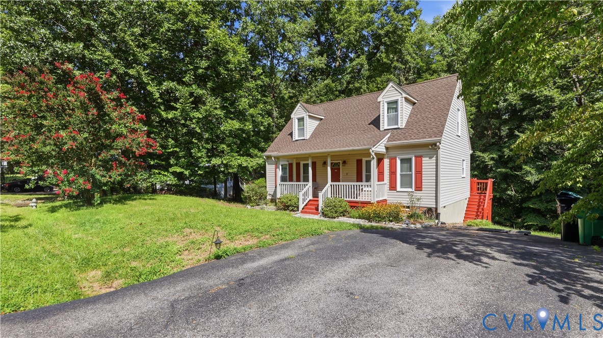 Cape Cod-style residence featuring a covered front porch, dual dormer windows, asphalt driveway, and exterior shutter accents