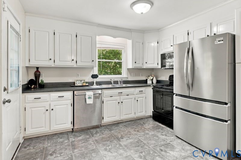 Kitchen featuring white cabinetry, solid-surface countertops, stainless steel dishwasher and refrigerator, black range, and tile flooring