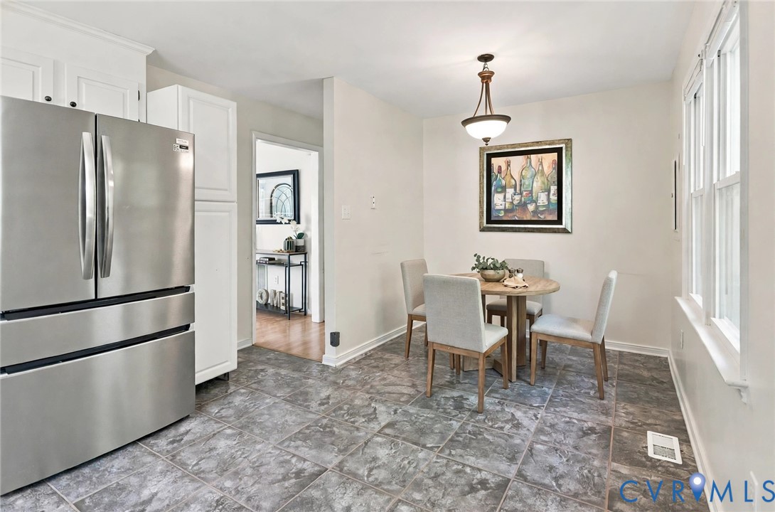 Eat-in area featuring ceramic tile flooring, shaker-style white cabinetry, stainless steel refrigerator, and pendant lighting