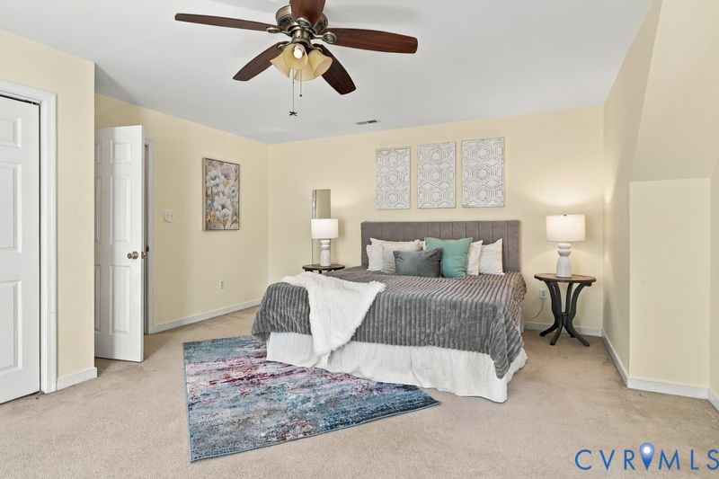 Spacious room featuring neutral wall paint, carpeted flooring, a ceiling fan with integrated light fixture, and a multi-panel interior door