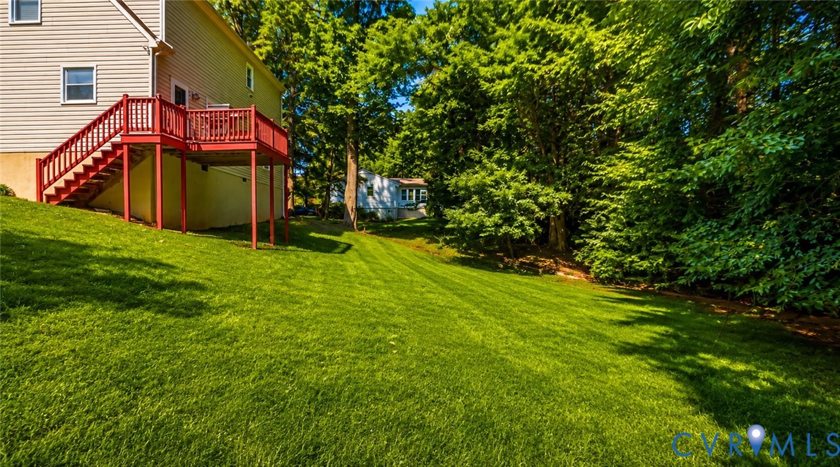 Expansive backyard featuring a tiered wooden deck with railing, sloping lawn, and perimeter mature trees