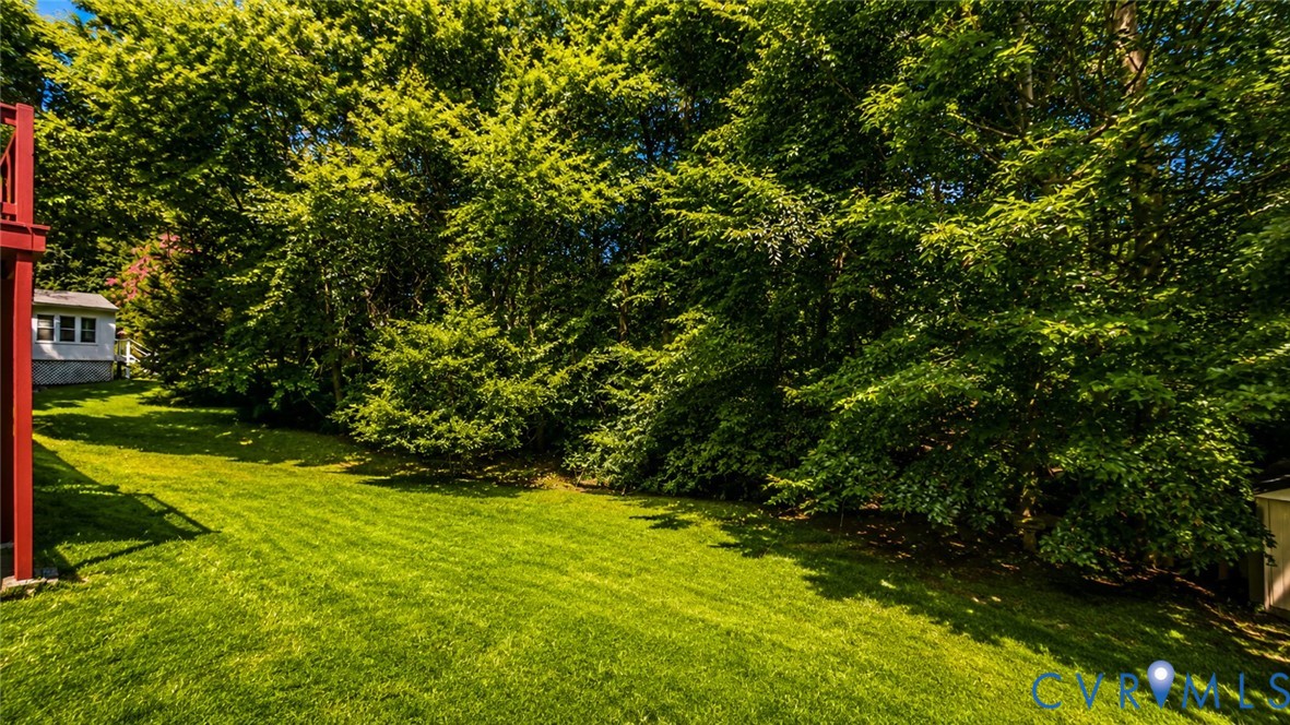 Expansive backyard featuring a manicured lawn, perimeter of mature trees, and an attached red deck structure