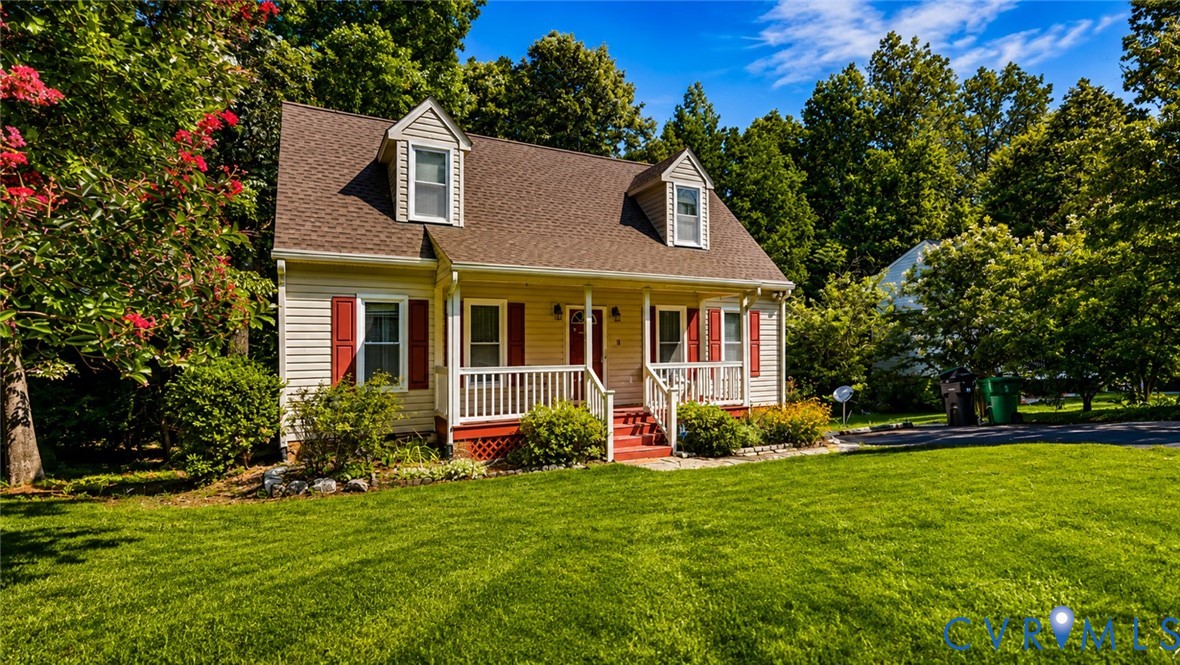 Cape Cod-style residence featuring horizontal siding, dual front-facing dormers, a covered front porch with railings, and decorative window shutters