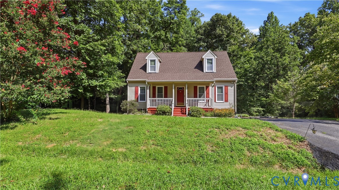 Two-story residence featuring a covered front porch, dual dormer windows, exterior shutters, and a sloped lawn