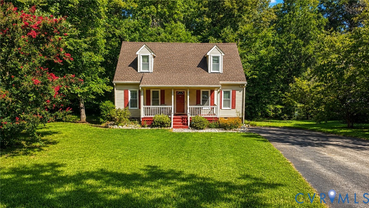 Cape Cod-style residence featuring light-colored siding, a covered front porch with railings, dormer windows, and a multi-gabled roofline
