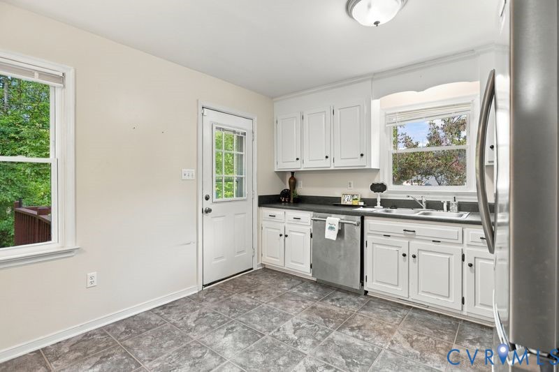 Kitchen featuring white cabinetry, dark stone-style countertops, stainless steel dishwasher, tile flooring, and a glass-paneled exterior door