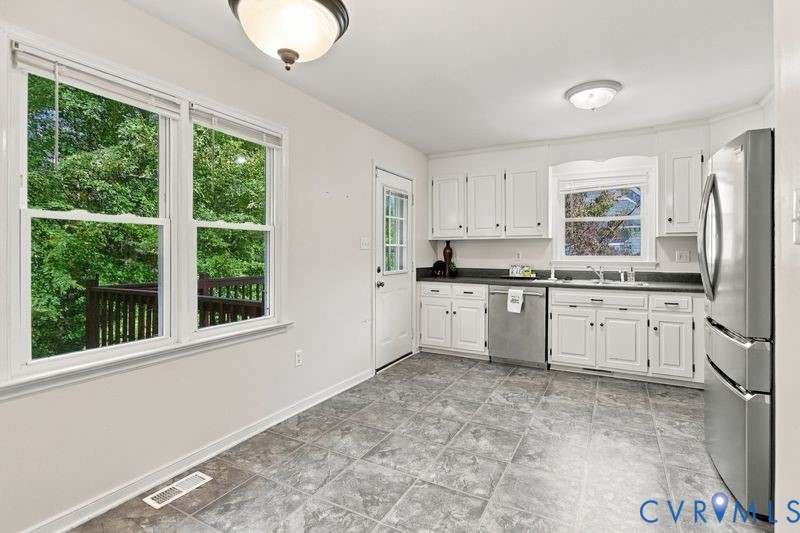 Kitchen featuring white cabinetry, stone-finish countertops, stainless steel appliances, tile flooring, and windows with natural light
