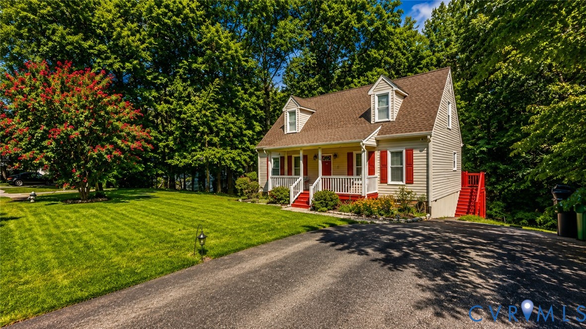 Cape Cod-style residence featuring a covered front porch, dual dormer windows, asphalt shingle roofing, and an attached side staircase