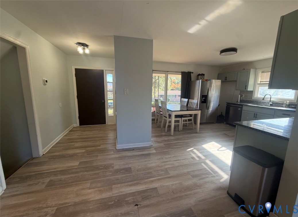 Open-concept interior featuring wood-finish flooring, cabinetry with stone-finish countertops, stainless steel appliances, and multi-pane front entry door