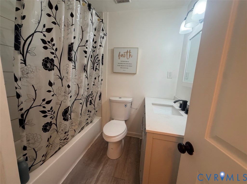 Bathroom featuring a vanity with a white countertop and rectangular integrated sink, matte black faucet, wood-finish flooring, and a shower-tub combination