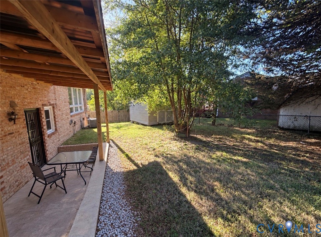 Backyard featuring a covered patio, brick exterior, stone-border landscaping, and mature trees