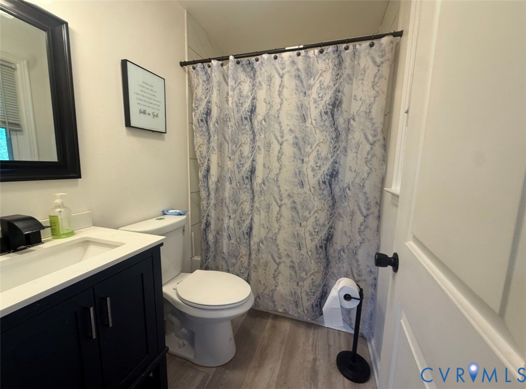Bathroom vanity with dark cabinetry, white countertop, rectangular basin, and black faucet fixtures, complemented by wood-finish flooring