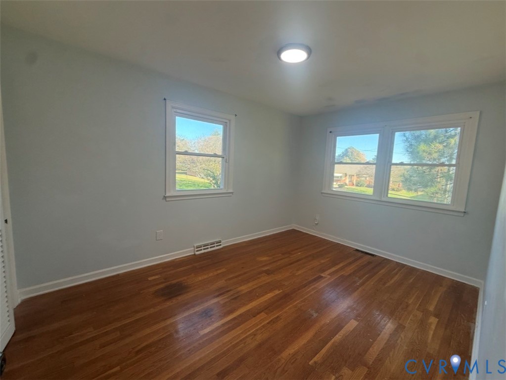 Room featuring wood-finish flooring, three windows with white frames, and a flush-mount ceiling light fixture