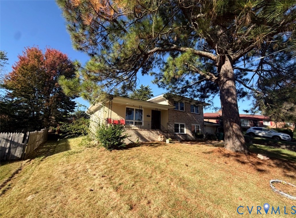 Split-level exterior featuring a brick and siding facade, covered front entryway, metal railing, and mature pine trees on the lot