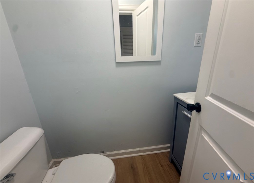 Bathroom featuring wood-finish flooring, a charcoal-toned vanity cabinet with a stone-top finish, a wall-mounted rectangular mirror, and a white toilet
