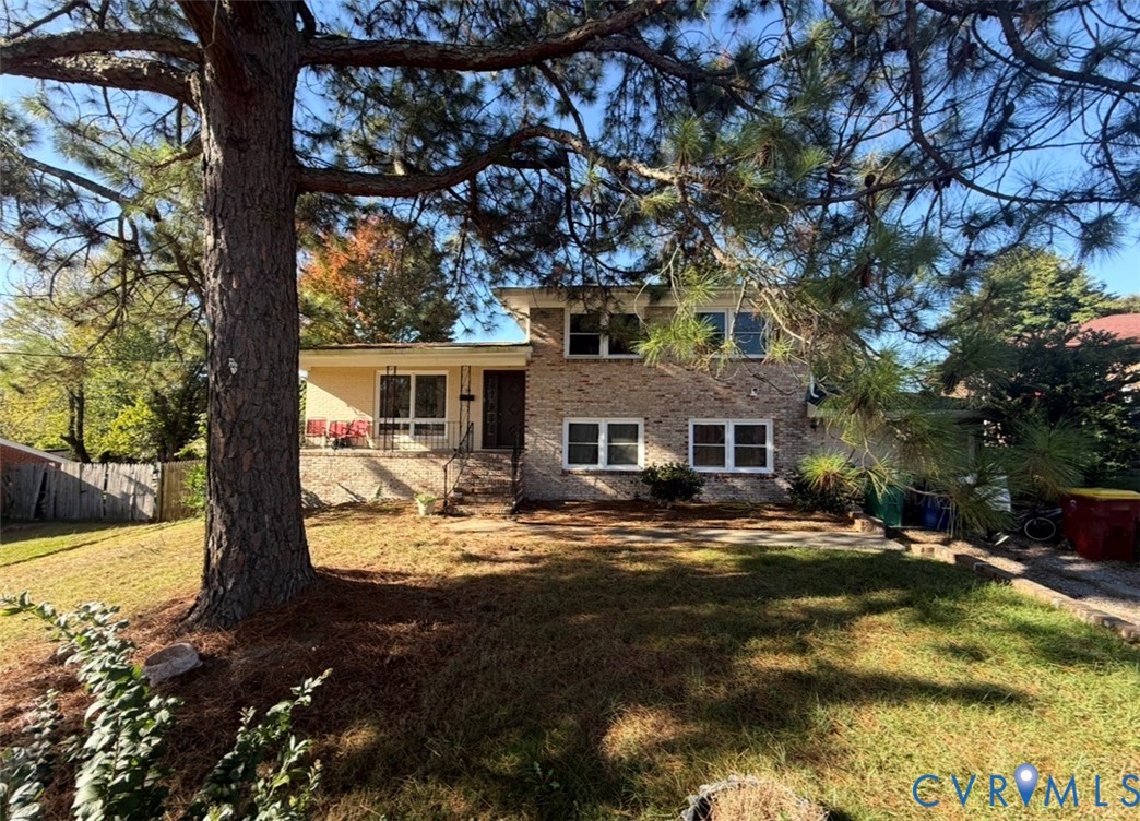 Split-level exterior featuring a brick and stucco facade, concrete front porch, and mature pine trees