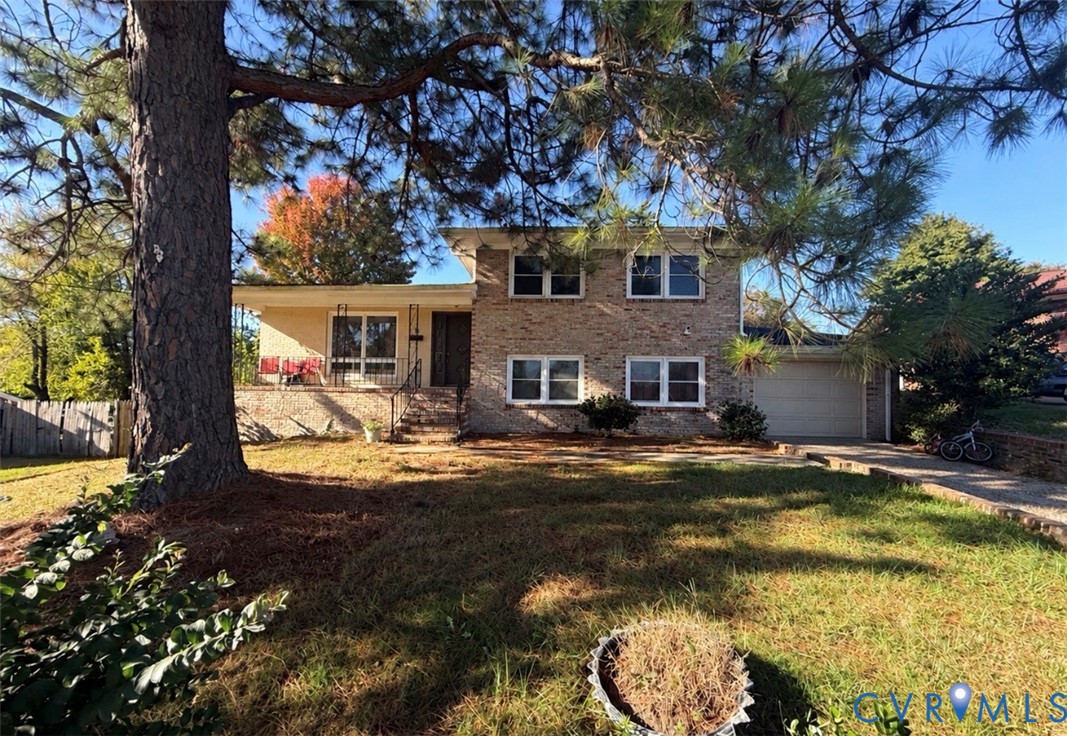 Split-level exterior featuring a brick facade, integrated garage, front porch with wrought-iron railing, and mature landscaping Split-level exterior featuring a brick facade, integrated garage, front porch with wrought-iron railing, and mature landscaping