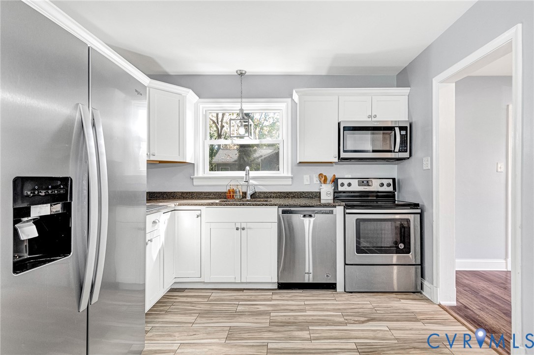 Kitchen featuring white cabinetry, stainless steel appliances, dark countertops, and wood-finish flooring Kitchen featuring white cabinetry, stainless steel appliances, dark countertops, and wood-finish flooring