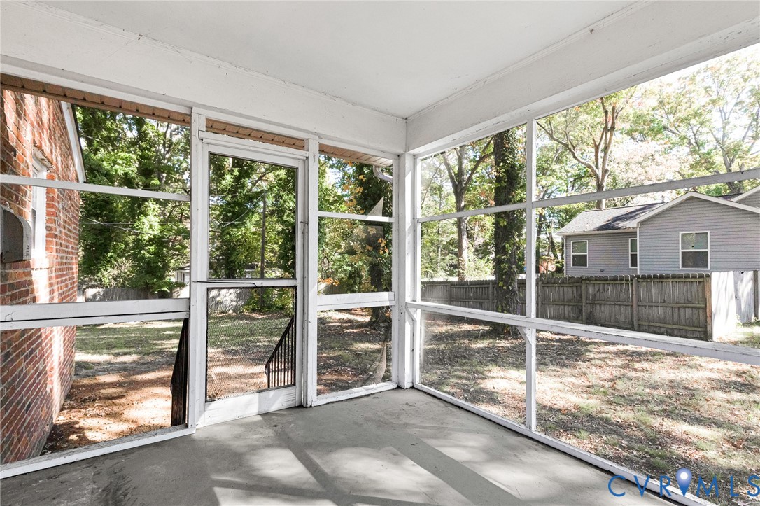 Screened-in porch featuring full-height window panels, a metal-framed storm door, concrete flooring, and an exterior brick wall