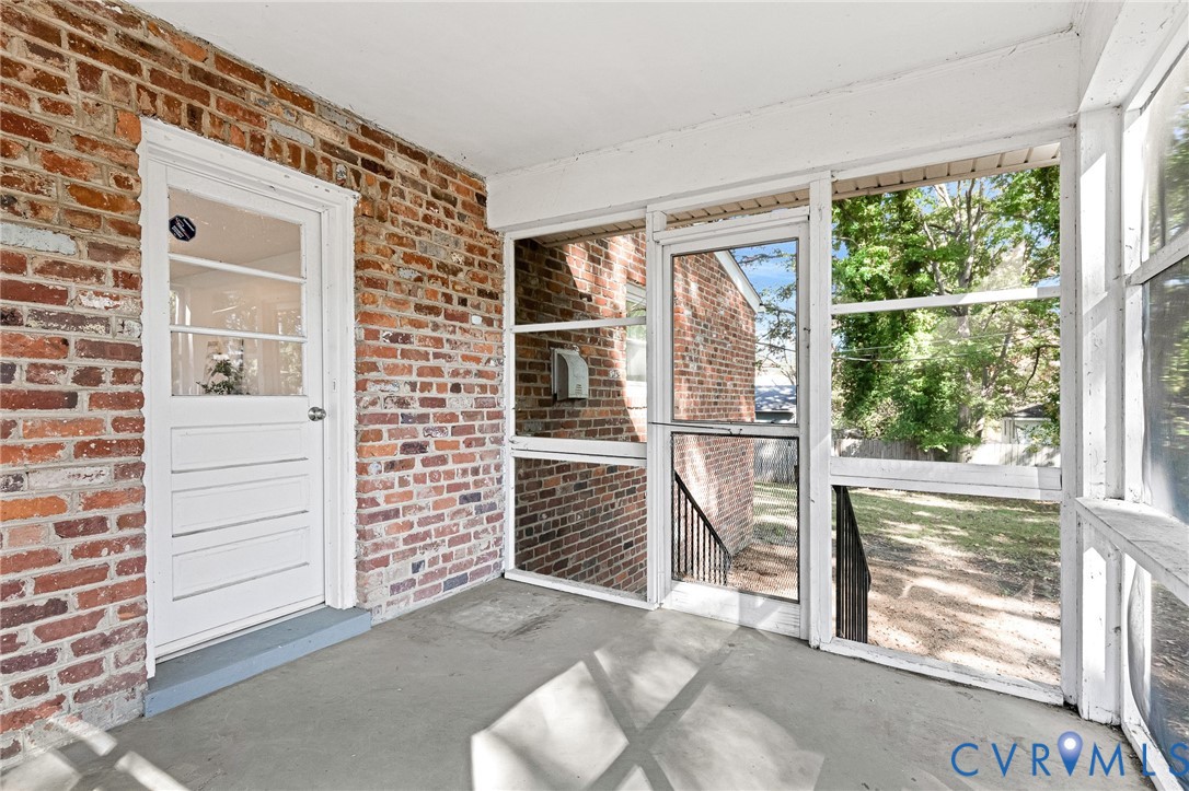 Screened-in porch featuring exposed red brick walls, concrete flooring, and a white-framed glass pane door