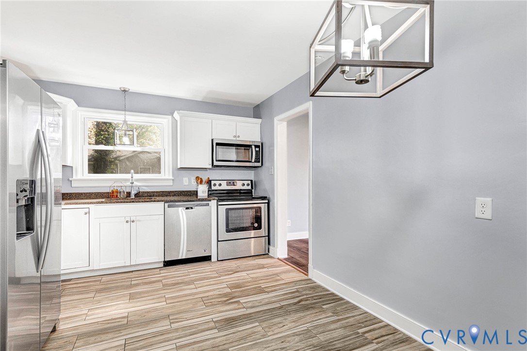Kitchen featuring white cabinetry, stainless steel appliances, wood-finish flooring, and a contemporary geometric pendant light