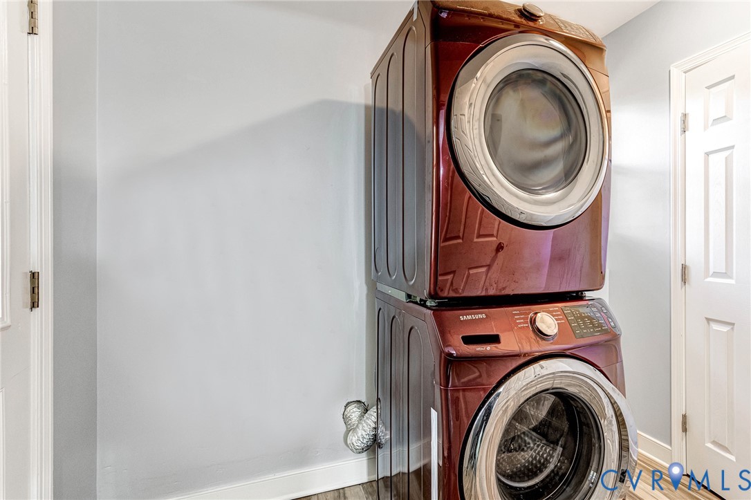 Stacked, front-loading laundry appliances with a high-gloss finish, multi-panel doors, and wood-finish flooring