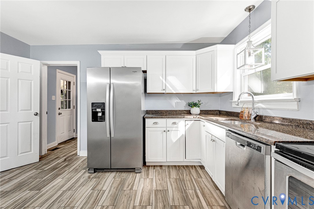 Kitchen featuring white shaker-style cabinetry, stone-surface countertops, stainless steel appliances, wood-finish flooring, and a pendant light fixture Kitchen featuring white shaker-style cabinetry, stone-surface countertops, stainless steel appliances, wood-finish flooring, and a pendant light fixture