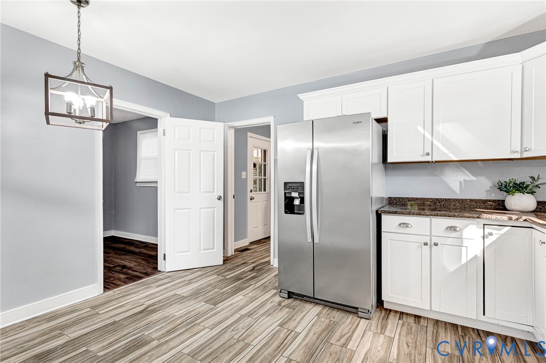 Kitchen featuring white shaker-style cabinetry, stone-finish countertops, stainless steel side-by-side refrigerator, multi-tone wood-finish flooring, and a geometric pendant light fixture Kitchen featuring white shaker-style cabinetry, stone-finish countertops, stainless steel side-by-side refrigerator, multi-tone wood-finish flooring, and a geometric pendant light fixture