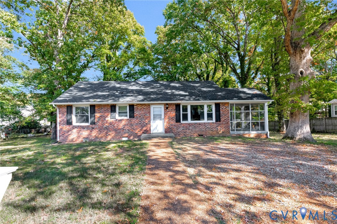Brick exterior residence featuring a front-facing screened porch, dark window shutters, and a gravel driveway