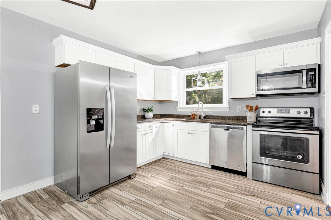 Kitchen featuring white cabinetry, wood-finish flooring, stainless steel appliances, and stone-finish countertops Kitchen featuring white cabinetry, wood-finish flooring, stainless steel appliances, and stone-finish countertops