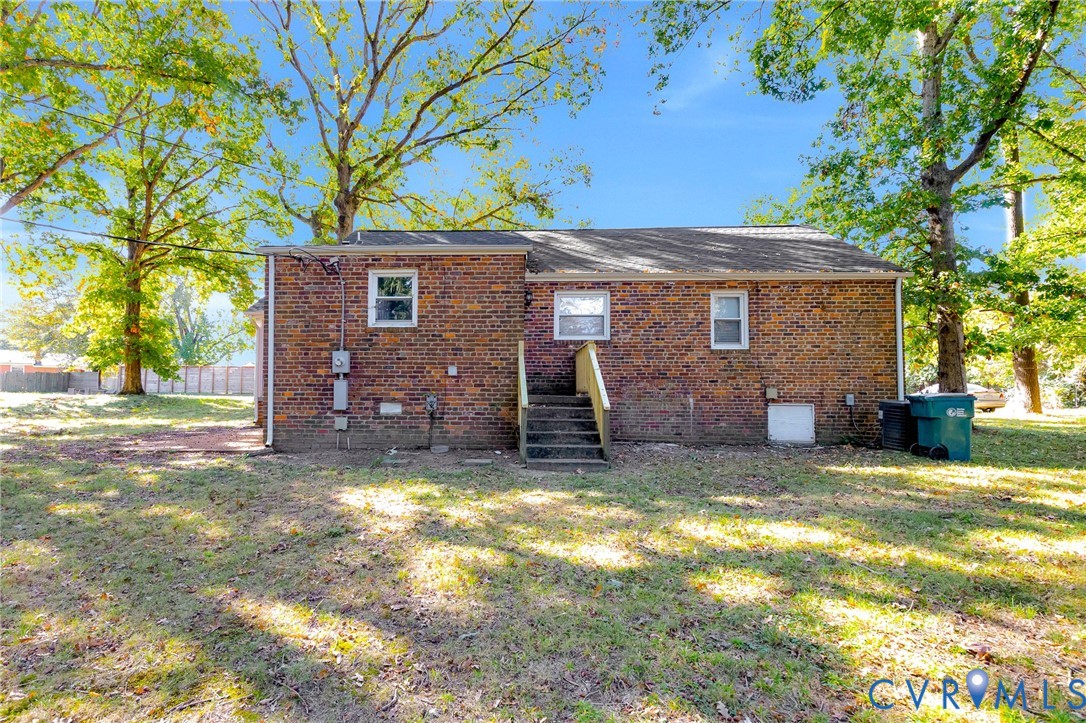 Full brick exterior featuring a shingle roof, wood stair entry, and mature trees on a level lot
