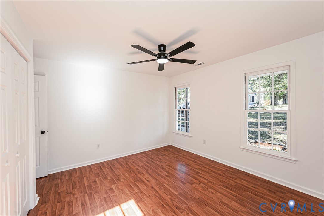 Interior room featuring wood-finish flooring, two double-hung windows, and a matte black ceiling fan with integrated lighting