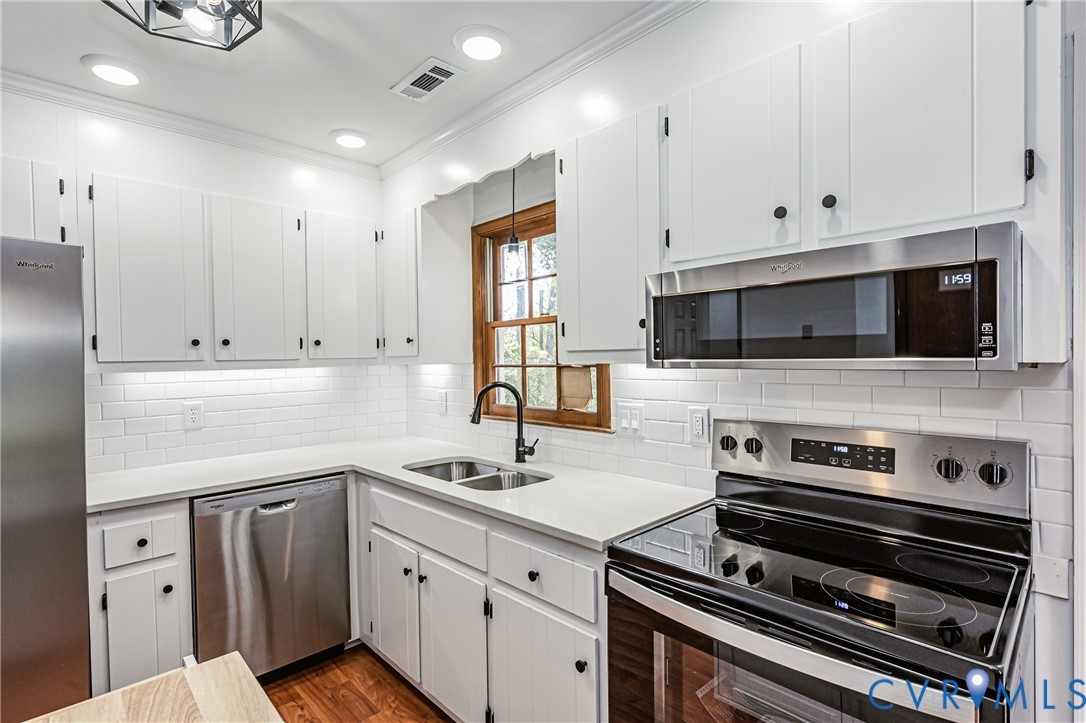 Kitchen featuring white shaker-style cabinetry, stainless steel appliances, solid surface countertops, a white subway tile backsplash, and a matte black faucet