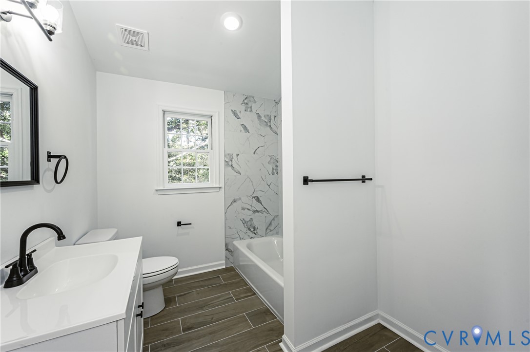 Bathroom featuring wood-finish flooring, a white vanity with a solid-surface countertop, matte black fixtures, and a tub surround with large-format decorative tile