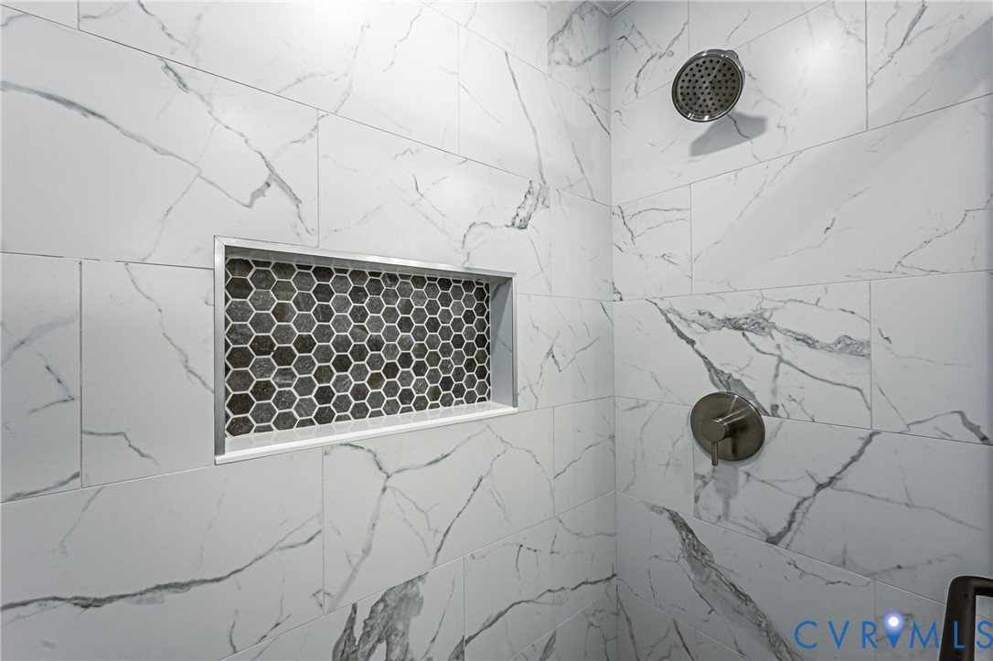 Shower featuring large-format tile with veining, an integrated recessed wall niche with hexagonal mosaic tile inlay, and polished metallic fixtures