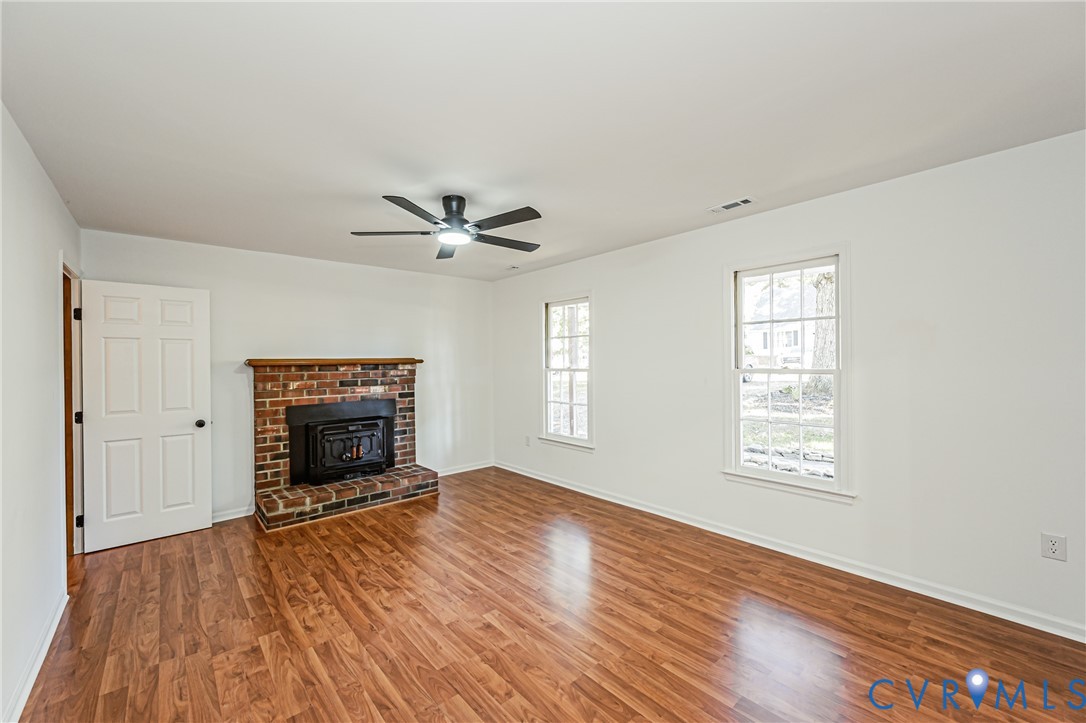 Living space featuring wood-finish flooring, a red brick fireplace with a wood mantle, a ceiling-mounted light fixture with fan, and double-hung windows