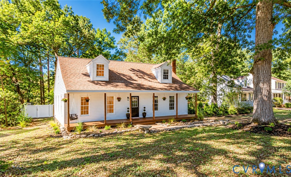Cape Cod-style residence featuring a full-width covered front porch, dual roof dormers, white siding, and stone hardscaping