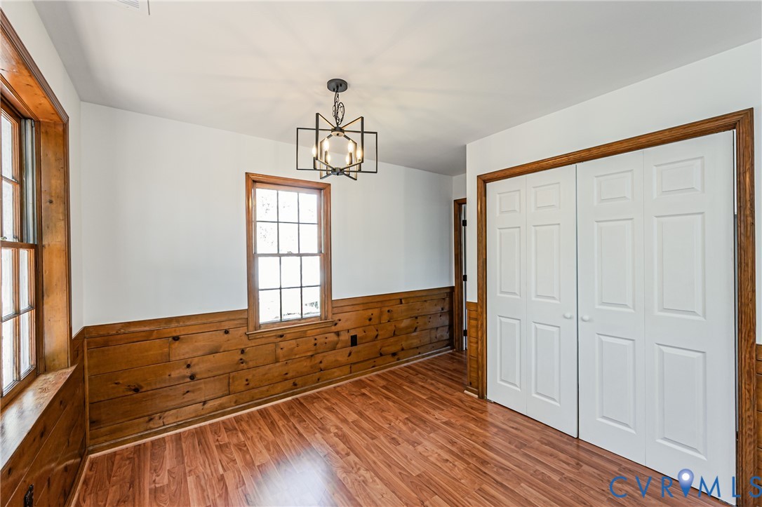 Room featuring wood-finish flooring, half-wall wood paneling, multi-pane windows with wood trim, six-panel closet doors, and a geometric-style metal pendant light fixture