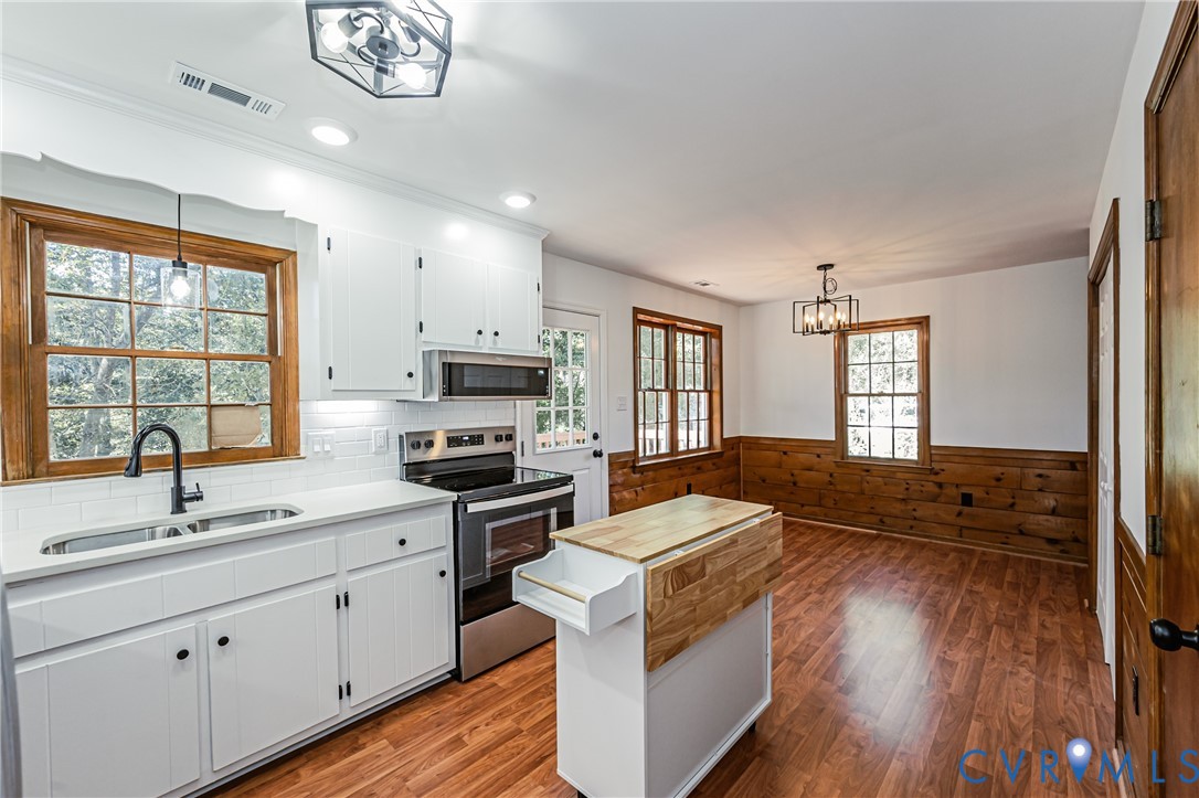 Kitchen featuring white cabinetry, subway tile backsplash, wood-finish flooring, stainless steel appliances, and wood-paneled walls