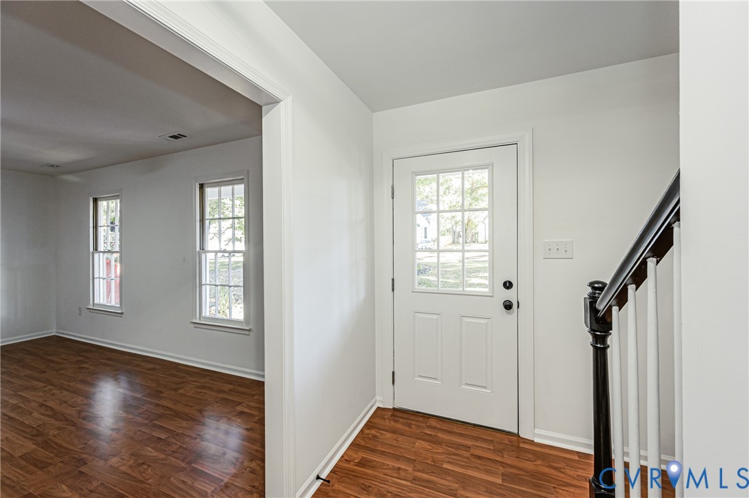 Entryway featuring wood-finish flooring, a six-pane glass inset entry door, and a staircase with a dark-finished newel post and white balusters