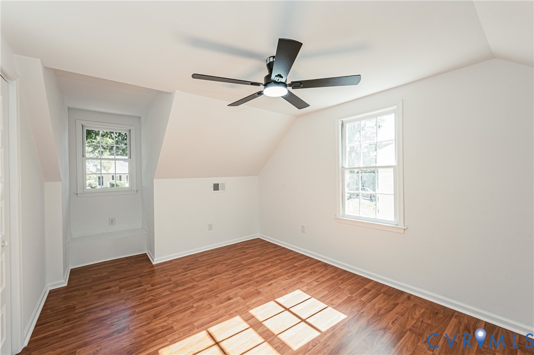 Room featuring wood-finish flooring, two double-hung windows, and a ceiling fan with integrated lighting